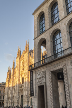 Palazzo monumentale in pietra con ampie arcate in primo piano, affacciato su una cattedrale gotica illuminata dal sole.