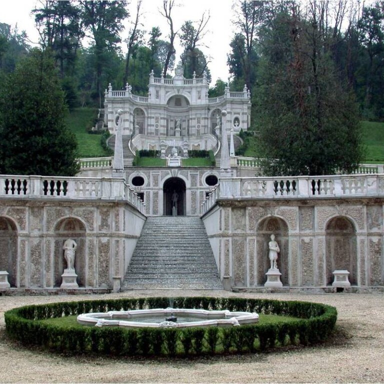 Scenografica struttura architettonica semicircolare in pietra su più livelli con fontana, scalinata centrale e nicchie con statue.