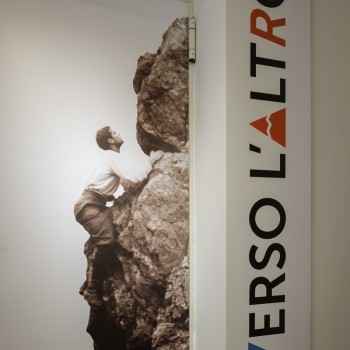 Foto in bianco e nero di Pier Giorgio Frassati intento ad arrampicare su una parete rocciosa, posta a fianco del logo del museo.